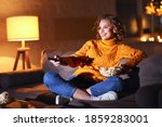 young  cheerful woman eating popcorn and watches  movie on  cable TV while switching channels with the remote control at home in evening  alone