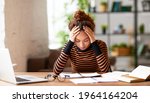 Small photo of Stressed young afro american woman holding head in hands and feeling demotivated while sitting at her home office and working remotely on laptop. Depressed female student tired of onling learning