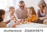 Small photo of Excited children playing game Jenga at home with positive senior grandparents while sitting on sofa in living room, two little girls and boy spending happy time with grandma and grandpa on weekend