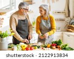 Small photo of Happy elderly couple smiling husband and wife in aprons prepare salad together at kitchen table, chopping variety of colorful vegetables, trying to maintain healthy lifestyle eating vegetarian food