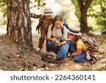 Small photo of Happy family: two kids boy and girl with backpacks looking examining environment through magnifying glass while exploring forest nature on sunny day during outdoor ecology school lesson