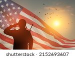 Small photo of USA army soldier saluting on a background of sunset or sunrise and USA flag. Greeting card for Veterans Day, Memorial Day, Independence Day. America celebration. Closeup. 3D-rendering.