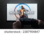 Small photo of Mortal Kombat 1 game on TV screen with gamepad in hand on black textured wall with light. Astana, Kazakhstan - July 2, 2023.