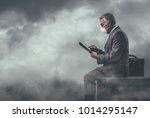 Businessman sitting on a rooftop in a polluted city and using a tablet: environmental pollution and business concept