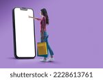 Happy woman doing online shopping using a big smartphone, she is holding shopping bags and touching the blank screen