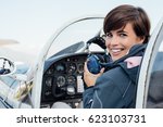 Smiling female pilot in the light aircraft cockpit, she is holding aviator headset and looking at camera