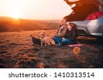 Father and daughter with small yellow dog camping on a hill while sitting on the ground by the car and having relaxing conversation