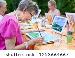 Side view of a happy senior woman smiling while drawing as a recreational activity or therapy outdoors together with the group of retired women.