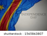 waving colorful national flag of democratic republic of the congo on a gray background with text independence day. concept