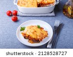 Small photo of Moussaka with meat, eggplant, tomatoes, potatoes, bechamel sauce and cheese on a white plate. Traditional Greek dish. Close-up.