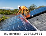Small photo of Solar panel technician with drill installing solar panels on house roof on a sunny day.