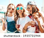 Three young beautiful smiling hipster female in trendy summer clothes.Sexy carefree women posing outdoors.Positive models holding and drinking fresh cocktail smoothie drink in plastic cup with straw