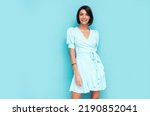 Portrait of young beautiful smiling female in trendy summer dress. Carefree woman posing near blue wall in studio. Positive model having fun indoors. Cheerful and happy. Isolated