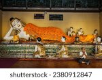 Small photo of YANGON, MYANMAR - JANUARY 3, 2014: Man meditating near statue of Recumbent Buddha in Shwedagon Paya pagoda