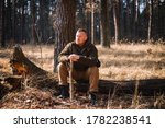 Small photo of Tough manhood forester sitting on the felled tree trunk in brown clothes