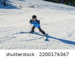 a little beginner skier on a ski slope in a funny inverted position and smiling behind the goggles looking at the camera, child having fun learning to ski, horizontal