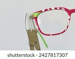 Small photo of Adjusting inclination on patchy red and white children eyeglass frame with conical nylon jaws inclination pliers.