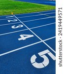 Small photo of Blue synthetic running track with 6 lanes, white starting line numbers 4 and 5, green turf infield, and orange cone at start line. Perfect for track and field events.