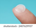 Small photo of Close-up round acne patch on finger on blue background. Acne patches for treatment of pimple and rosacea close-up. Facial rejuvenation cleansing cosmetology