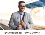 Young businessman on railroad station is eating sandwich. 