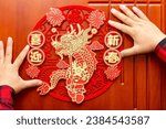 man sticking a Chinese New Year of the Dragon decoration to a door at horizontal composition translation of the Chinese words are fortune and welcome to the new year no logo no trademark