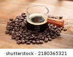 Espresso coffee in a wooden handle measuring cup the scale shows 60 millilitres or 2 ounce, It is double shots of espresso coffee with coffee beans on space of old wood background