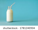 Small photo of Fresh farm milk in glass bottle with pink color tubule on blue background front view. Milk in glass bottle to the top close up. Fresh farm milk is good for children's health and saturates the body wi