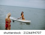 Small photo of Two pretty young women in the sea with addle board on a summer day
