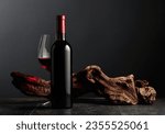 Bottle and glass of red wine on a black stone table. In the background old weathered snag. Frontal view with copy space.