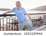 Small photo of Warm up firstly. Concentrated unshaken strong man standing on the quay holding by the railings and stretching his leg.