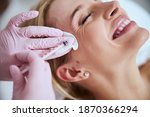 Small photo of Smiling lady lying with her eyes closed during the rejuvenation injection administered by a professional dermatologist