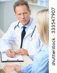 Small photo of Listen attentively. Serious agreeable professional doctor sitting at the table and listening to his patient while being involved in work