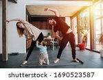 Small photo of The family practices yoga, family life in isolation. Mom and dad are doing exercises, and infant child creeps next to his parents. Sunset light from the windows. Family quarantine
