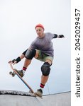 Small photo of Confident mature skater in a watch cap starting his roll in a skate park. Upward angle, tipping borad, leaning froward.