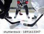 Small photo of Hockey referee with puck standing on ice rink with two rivals with sticks on his right and left waiting for moment to shoot it