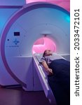 Small photo of Young patient covered with blue towel undergoing medical examination in magnetic resonance imaging scan machine