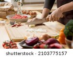Small photo of Hands of young female chopping fresh onion on wooden board while preparing italian pasta with vegetables and minced meat
