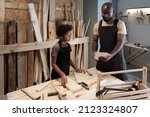 Small photo of Portrait of African-American father teaching son carpentry while working together in woodworking shop