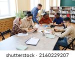 Small photo of Mature Caucasian English language teacher helping immigrant students with doing task during lesson in library