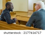 Small photo of Young African American pastor consulting senior male parishioner after church service while both sitting on bench in front of one another