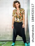 Small photo of Hispanic American Artist with brown curly hair in New York City, wearing colorful patterned short sleeve shirt, baggy loose pants with suspenders, patterned sneakers, hanging old key as necklace.