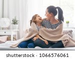 A nice girl and her mother enjoy sunny morning. Good time at home. Child wakes up from sleep. Family playing under blanket on the bed in the bedroom.