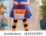 Happy Halloween! Little kid with a basket for sweets  wearing face mask protecting from COVID-19.