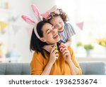 Small photo of Happy holiday! Mother and her daughter with painting eggs. Family celebrating Easter. Cute little child girl is wearing bunny ears.