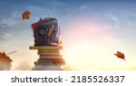Small photo of Back to school! Backpack is standing on the tower of books on background of sunset sky. Concept of education and reading.