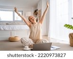 Happy casual beautiful woman working on a laptop sitting on the floor in bedroom at home.