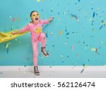 Little child plays superhero. Kid on the background of bright blue wall. Girl is throwing confetti and jumping. Yellow, pink and  turquoise colors.