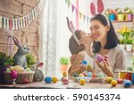 Mother and her daughter painting eggs. Happy family preparing for Easter. Cute little child girl wearing bunny ears.