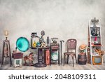 Antique gramophone, chair, retro microphone and recorder on table. Old telephone, typewriter, radio, TV on shelving front concrete wall background. Nostalgic still life. Vintage style filtered photo