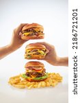 Small photo of Two hands holding a gourmet cheese burger on top of one another with beef burger with potato chips on the bottom